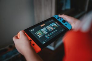 Člověk držící Nintendo Switch v čeveno-modré barvě