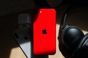 červený iPhone SE 2022 na zátiší se sluchátky a příslušenstvím