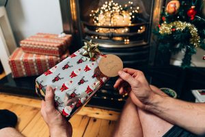 Muž rozbalující dárek pod vánočním stromečkem na Vánoce