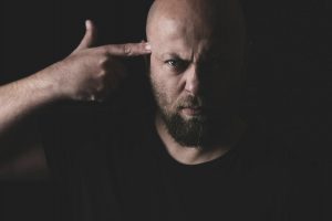 Muž v černém tričku si míří vlastním prstem na hlavu
