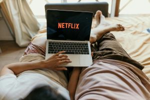 Pár ležící v posteli a sledující Netflix na počítači