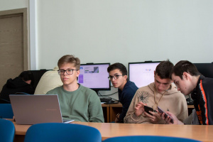 Žáci v počítačové učebně, dva používají smartphony a další pracují na notebooku a stolních počítačích
