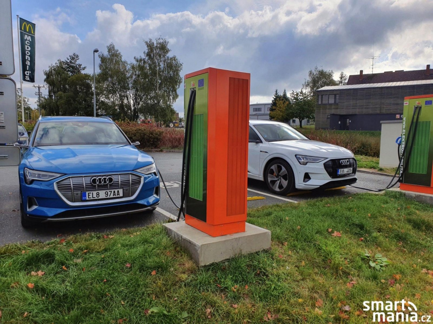 Elektromobily u veřejné nabíječky Modré a bílé Audi e-tron stojí u veřejných nabíjecích stojanů