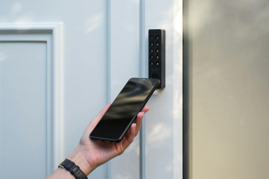 Klávesnice Nuki Keypad 2 NFC s telefonem u dveří Telefon přiložený ke klávesnici Nuki Keypad 2 NFC na vstupních dveřích