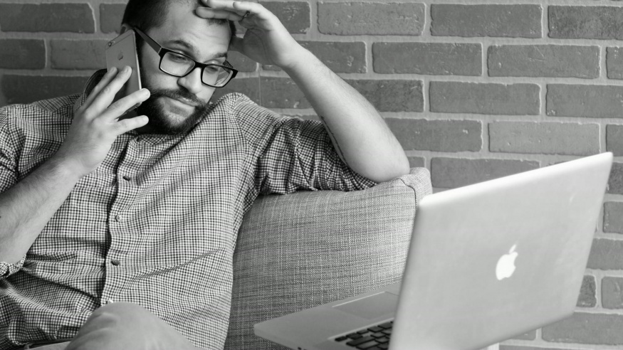 Podezřelý telefonát u MacBooku Znepokojený muž telefonuje a sleduje MacBook