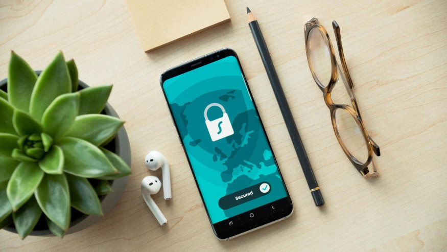Telefon se symbolem zabezpečení Telefon se symbolem zámku leží na stole vedle sluchátek a brýlí