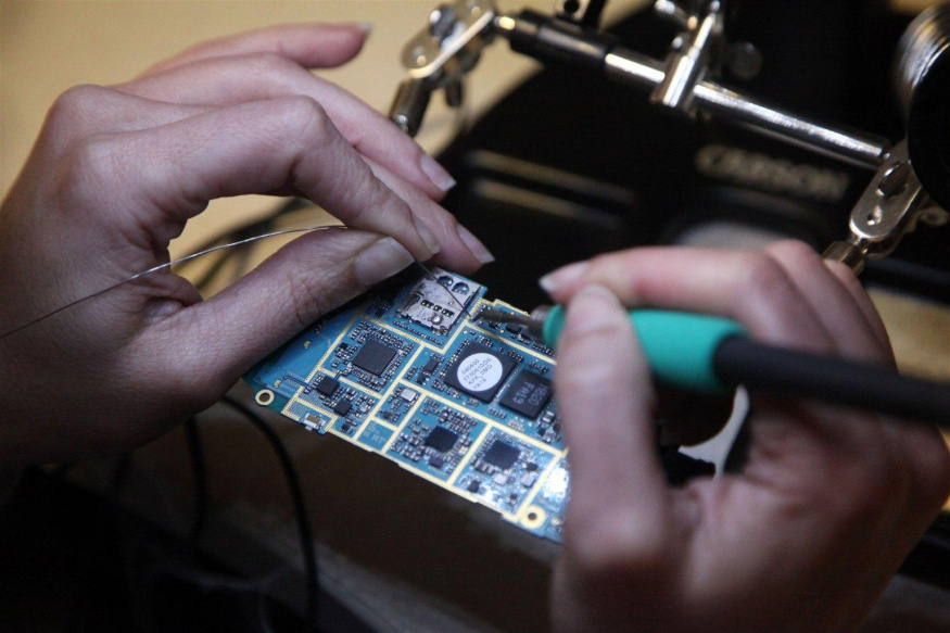 JTAG přístup k desce telefonu Ruce specialistky pájejí vodič k desce rozebraného mobilního telefonu
