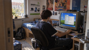 Mladý člověk sedí u počítače s CRT monitorem v dobově zařízeném pokoji