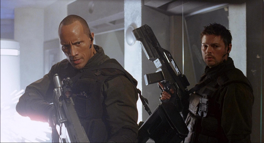 Mariňáci ve filmu Doom Dwayne Johnson vlevo a Karl Urban vpravo v tmavé bojové výstroji se zbraněmi uvnitř stanice