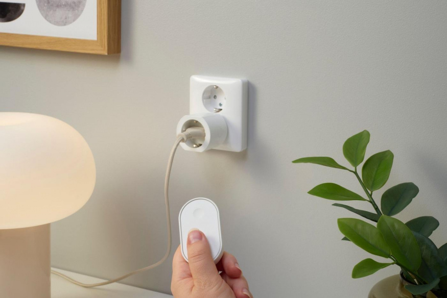 Chytrá zásuvka IKEA GRILLPLATS Chytrá zásuvka IKEA GRILLPLATS ve zdi vedle lampy a ruka s ovladačem