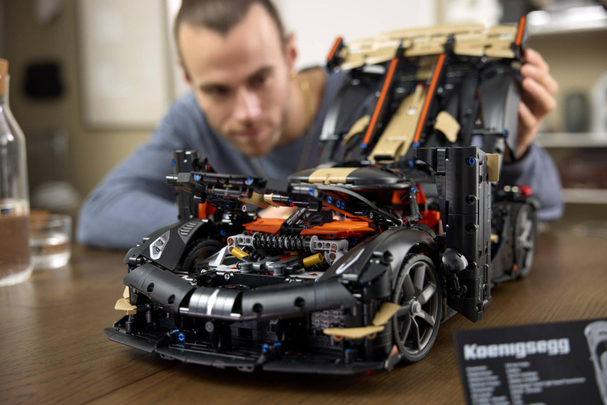 Koenigsegg Sadair’s Spear v režimu Ghost Mode Černozlatý LEGO Koenigsegg s otevřenými dveřmi, přední kapotou a vysoko zvednutým zadním krytem, který drží muž za modelem