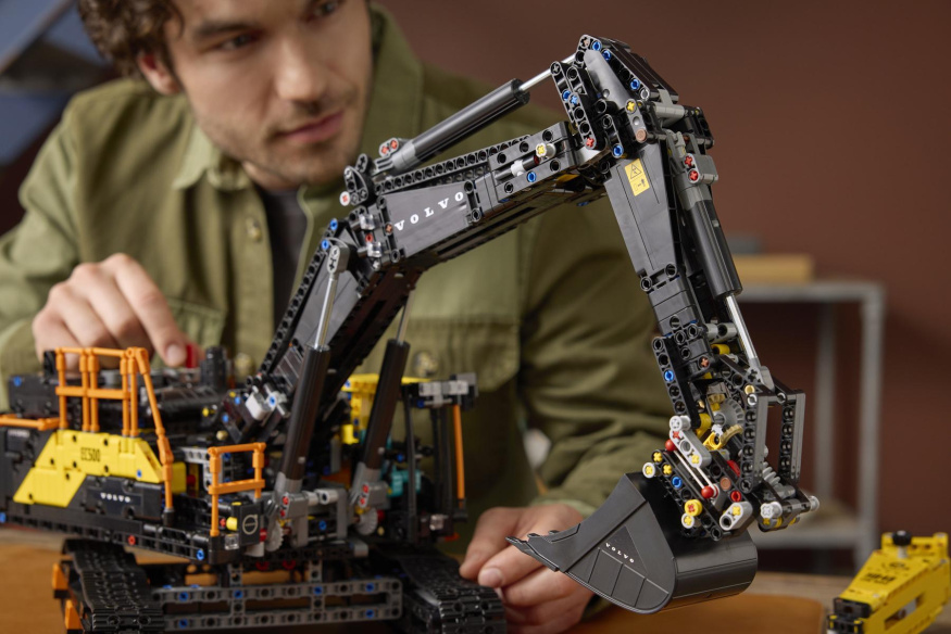 Ovládání ramene bagru Volvo EC500 Detail LEGO bagru Volvo EC500 se zdviženým ramenem a lžící, muž má prst na ovladači nástavby