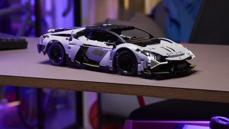 LEGO Lamborghini Revuelto s rozsvícenými světly Bílošedé LEGO Lamborghini Revuelto s rozsvícenými předními světly na stole ve fialově nasvíceném pokoji