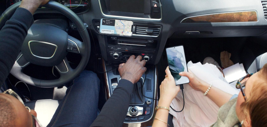 Nabíjení dvou telefonů v interiéru auta Interiér auta s telefonem s navigací na palubní desce a druhým připojeným telefonem v rukou spolujezdkyně