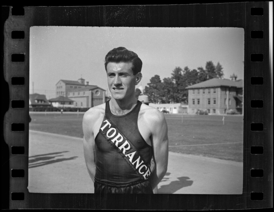 Louis Zamperini na Bovard Field, 1938 Černobílý portrét Louise Zamperiniho v atletickém dresu Torrance na sportovním hřišti
