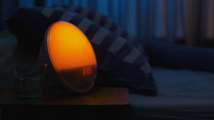 Světelný budík v tmavé ložnici Oranžově rozsvícený budík Philips na nočním stolku v tmavé ložnici